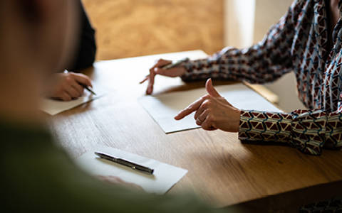 Close shot of three people around a table. They have pens and paper in front of them