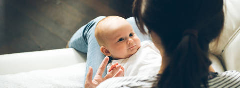 Baby smiling up at mother with dark hair in ponytail.